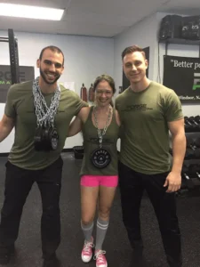 Three fitness enthusiasts in gym attire, posing with weights and chains.